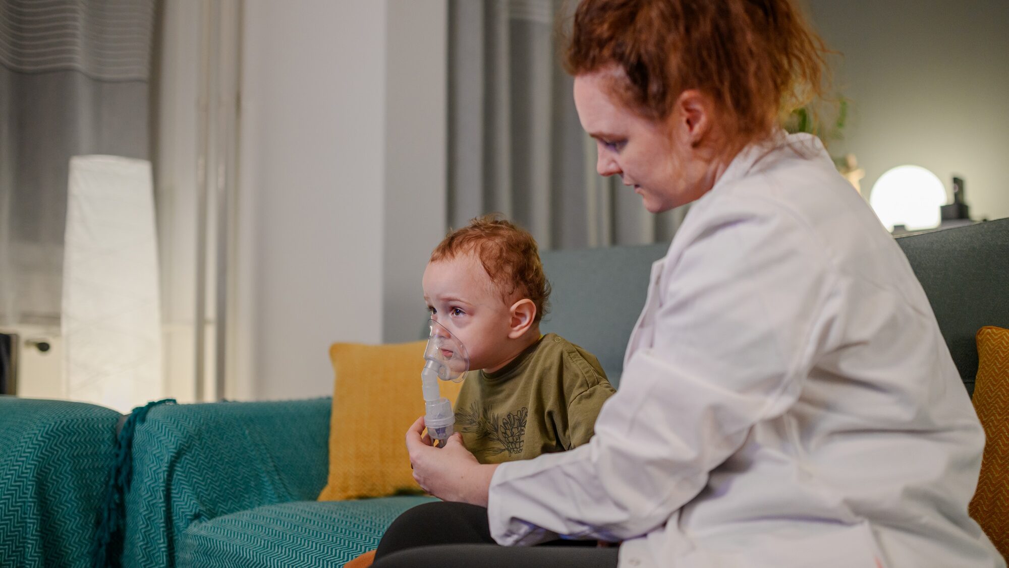 Doctor with a sick toddler breathing through mask at home.