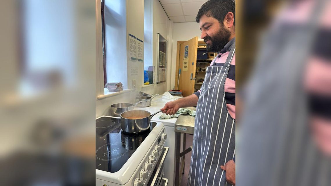 A man cooking in a class, stirring a pot on the stove.