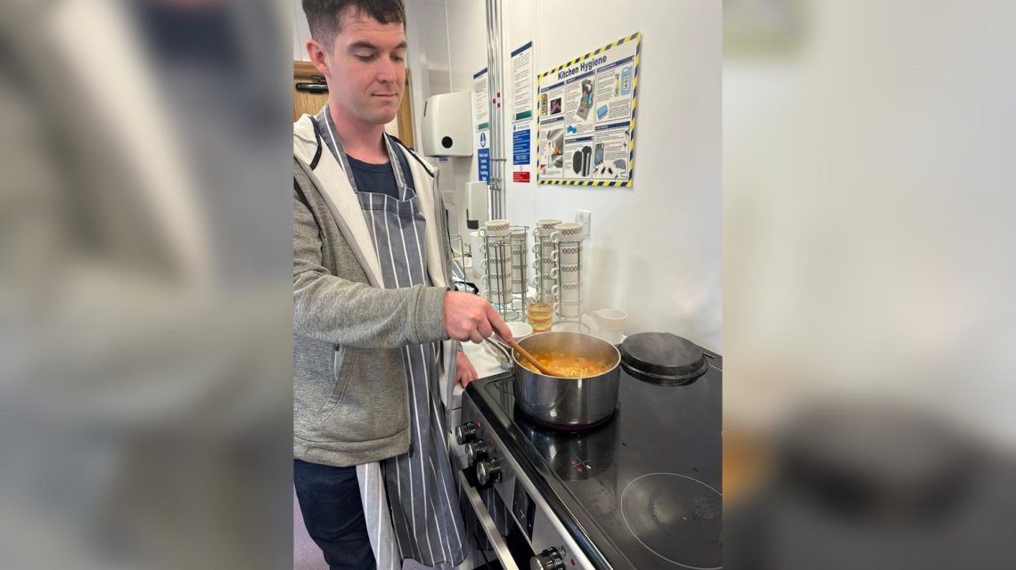 A man is cooking in a kitchen, stirring a pot on the stove.