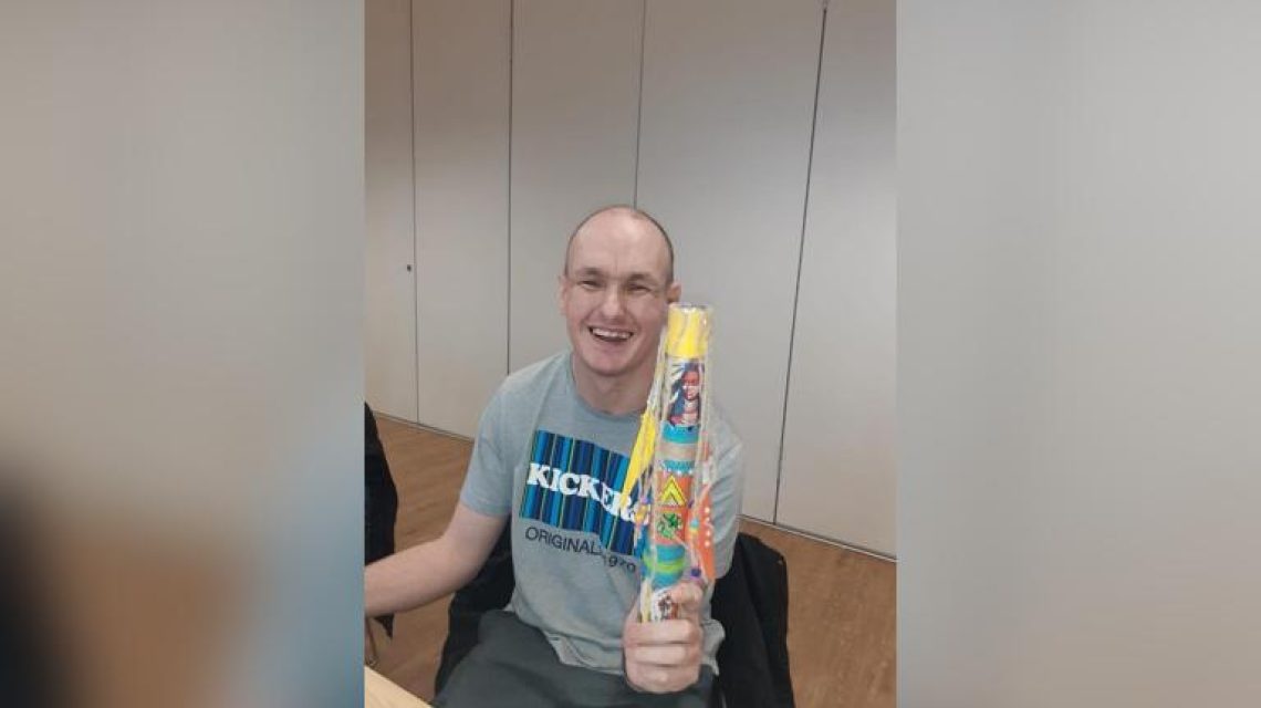 A man proudly displaying a colourful handmade craft.