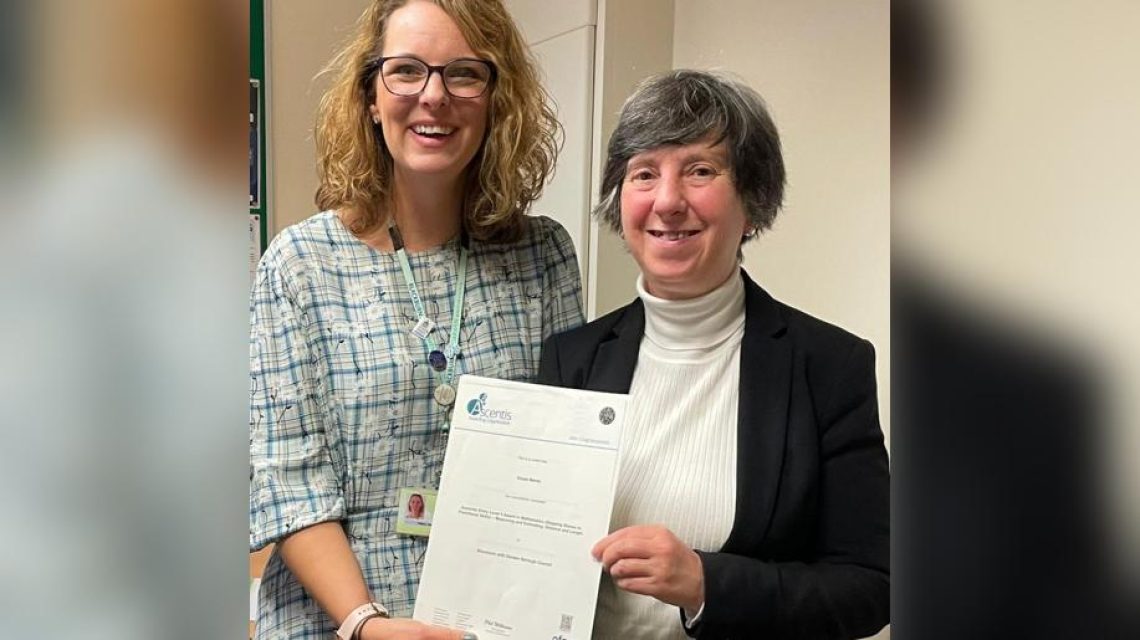 The image shows two women standing side by side holding a certificate.